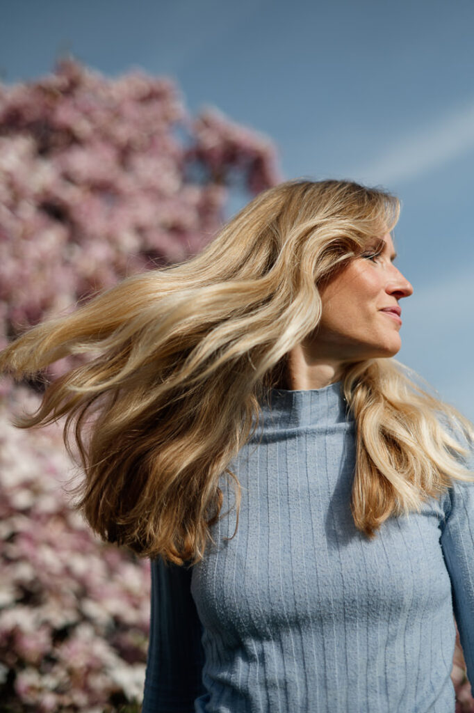 Blonde Frau mit wehendem Haar vor Magnolienbaum
