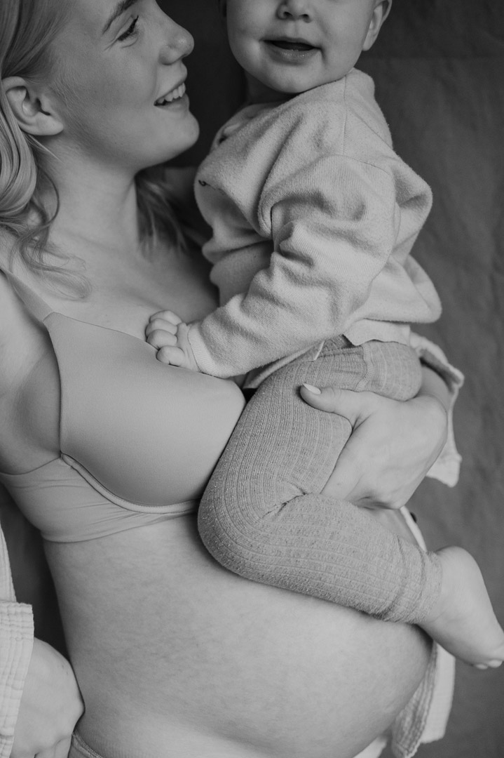 Kleinkind sitzt auf Babybauch im Arm der Mama