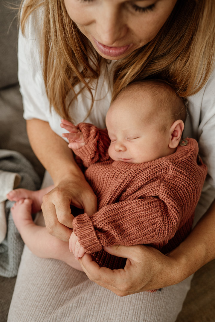 Baby in rostroten Pullover liegt in Mamas Armen auf dem Schoss