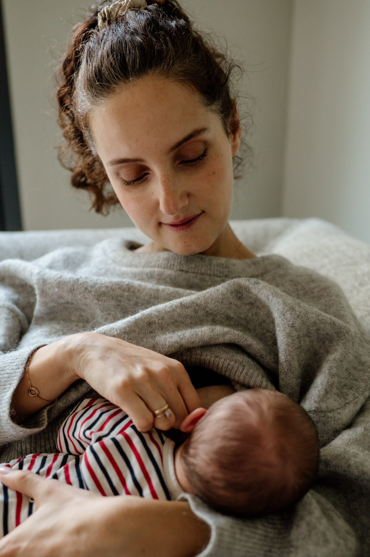 Frau in Pullover schaut liebevoll auf Ihr Baby während sie es stillt